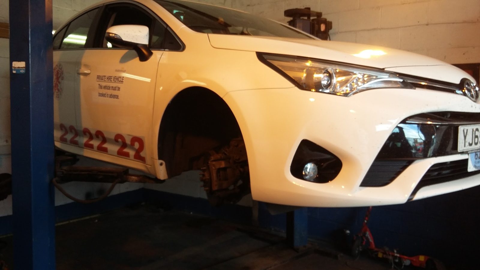 A white Toyota raised on the lift with a front wheel off