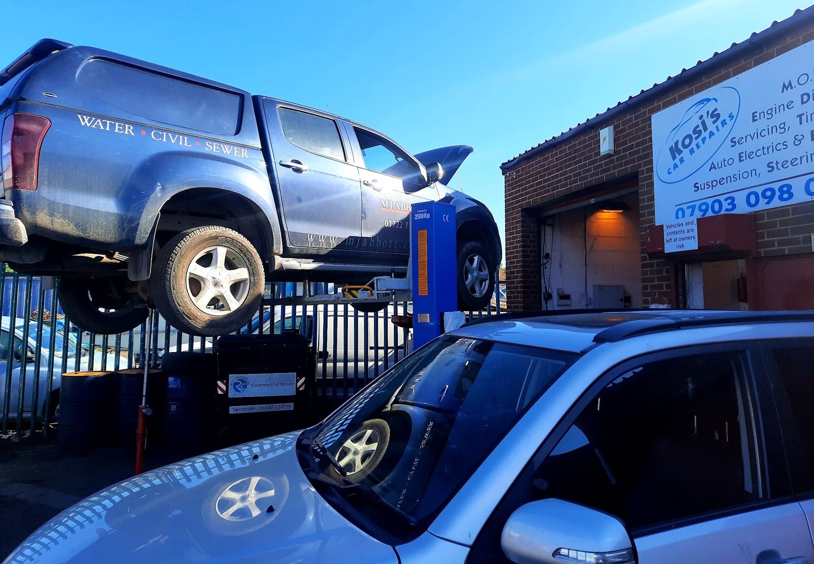 Outside Unit 12, Teal Court: a pickup raised on a lift beside the Kosi's Car Repairs sign