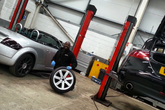 A mechanic holding an alloy wheel between two cars in the workshop